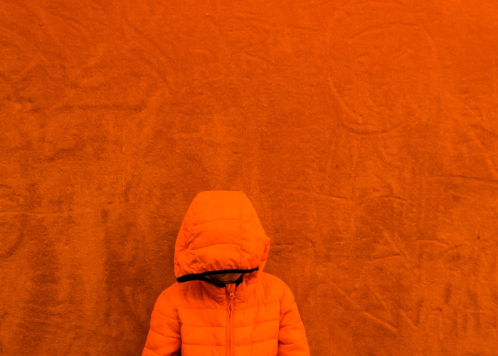 Orange jacket boy in front of orange wall diana hagues photograp